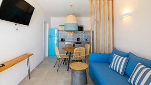 A compact living space with a kitchenette, a dining area with chairs, a sofa with striped pillows, and a television mounted on the wall.