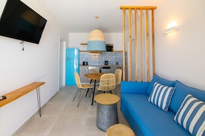 Ett kompakt bostadsutrymme med ett litet kök, en matplats med stolar, en soffa med randiga kuddar och en tv som är monterad på väggen.