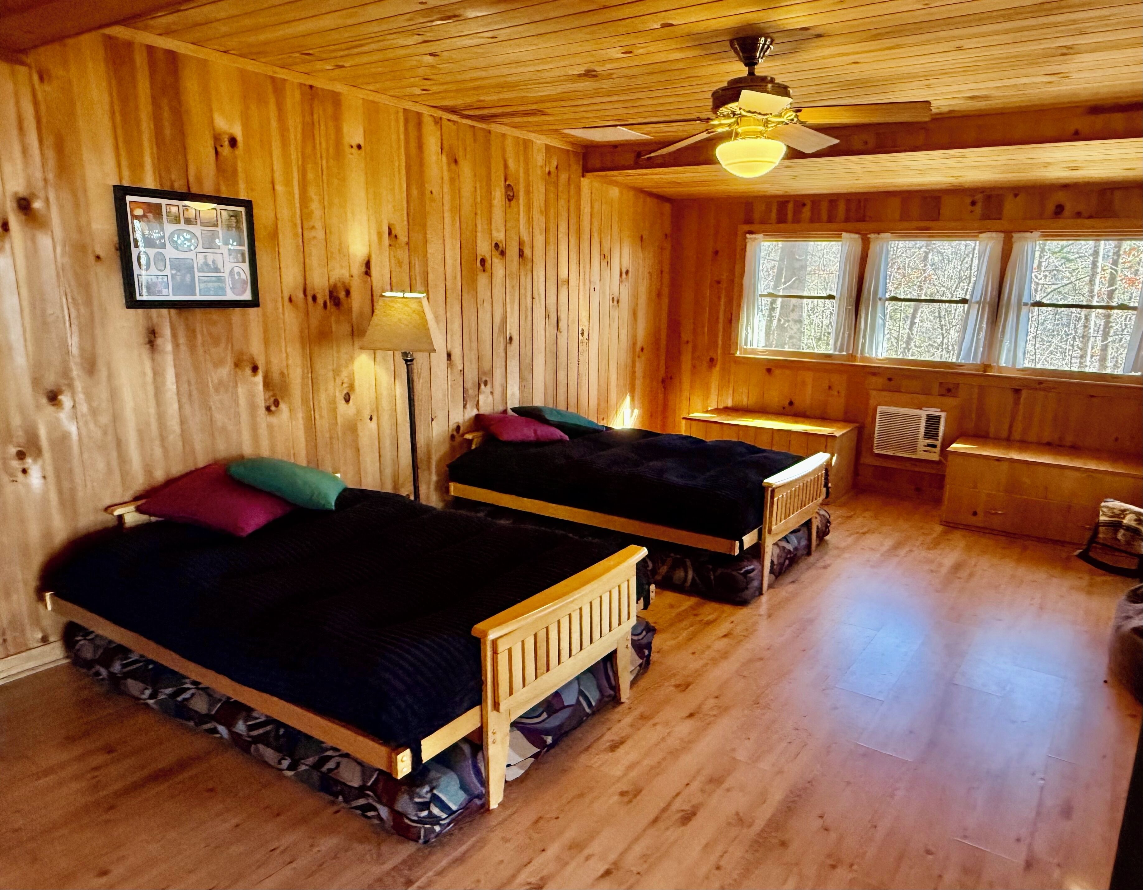 A cabin with two wooden beds, a ceiling fan, and a framed photo on the wall.