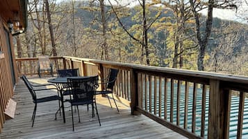 A wooden deck with outdoor furniture, overlooking a forested area with mountains in the background.