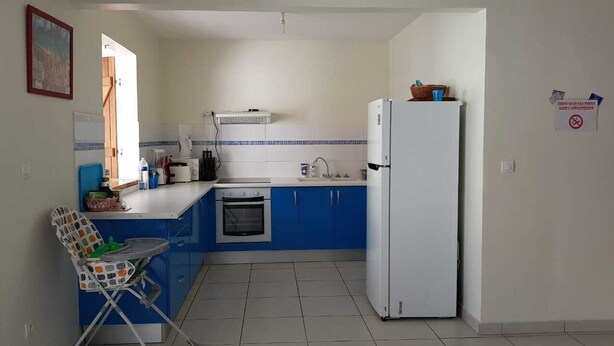 Una cocina compacta con armarios azules, un refrigerador blanco, un horno pequeño y un comedor con una trona.