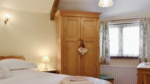 A bedroom with a bed, a wooden wardrobe, a nightstand with a lamp, a radiator, and a window with curtains. - 2 bedroom accommodation in Whitehaven (Whitehaven)