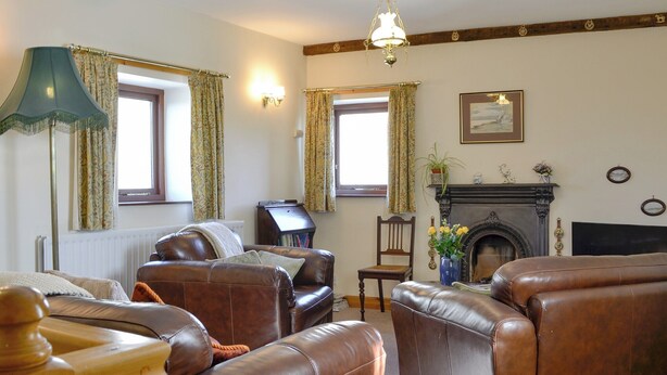 A living room with leather sofas, a fireplace, and a bookshelf. - 2 bedroom accommodation in Whitehaven (Whitehaven)