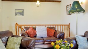 A living room with a brown leather sofa, a wooden headboard, a green floor lamp, and a vase with yellow flowers. - 2 bedroom accommodation in Whitehaven (Whitehaven)