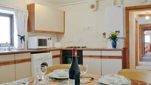A kitchen with a microwave, toaster, and sink. There is a dining table with plates, wine glasses, and a bottle of wine. - 2 bedroom accommodation in Whitehaven (Whitehaven)