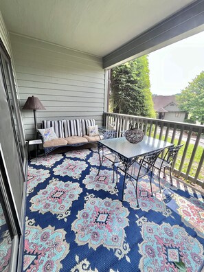 A covered porch with a patterned rug, a bench with cushions, and a table with chairs.