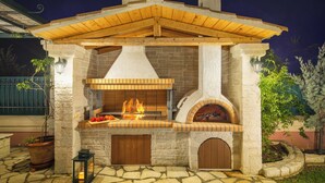An outdoor stone and wood-built barbecue area with a chimney, a fire pit, and a lantern. - Villa Rose Corfu, Villa (Acharavi)