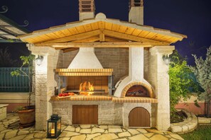 An outdoor stone and wood-built barbecue area with a chimney, a fire pit, and a lantern. - Villa Rose Corfu, Villa (Acharavi)