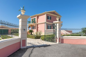 A pink villa with a gated entrance, a balcony, and a clear blue sky.
