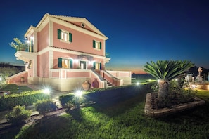A two-story house with a balcony, a staircase, and a well-lit garden area at night. - Villa Rose Corfu, Villa (Acharavi)