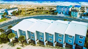 A coastal hotel with multiple blue buildings, a road in the foreground, and a beach in the background.