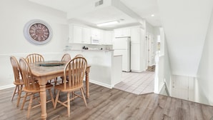 A modern kitchen with white cabinetry, a dining table with wooden chairs, and a wall clock.