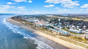 An aerial view of a coastal town with beachfront properties, a prominent water tower, and a long pier extending into the ocean.