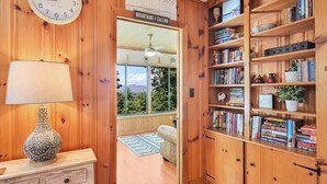 A wooden interior with a bookshelf, a wall clock, and a view through a window. - Spectacular Views! -Great Location-Hot Tub-Dreamy Porch & Sun Room-Fenced Yd! (Arden)