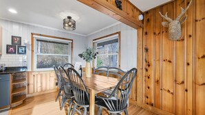 A wooden-paneled dining room with a wooden table and chairs, a vase with flowers, and a mounted animal head on the wall. - Spectacular Views! -Great Location-Hot Tub-Dreamy Porch & Sun Room-Fenced Yd! (Arden)