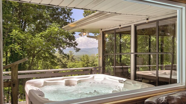 A hot tub with a wooden deck and glass walls, surrounded by lush greenery and a scenic view. - Spectacular Views! -Great Location-Hot Tub-Dreamy Porch & Sun Room-Fenced Yd! (Arden)