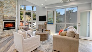 A spacious living room with a fireplace, comfortable seating, and large windows offering a view of the outdoors.