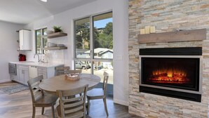 A modern kitchen with a large window, a fireplace, and a dining area with a round table and chairs.