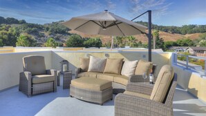A rooftop terrace with wicker furniture, including a sofa, chairs, and an ottoman.