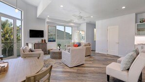 A spacious living area with a large dining table, two sofas, and a ceiling fan.