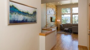 A modern interior with a large abstract painting, a wooden reception desk, a sofa, and a view of greenery through large windows. - Hawks Landing - New, Modern, Views, Billiards! (Hood River)