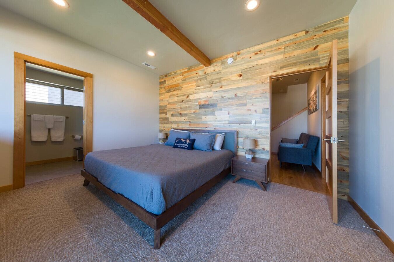 Quarto com parede em madeira, cama com roupa de cama azul, mesa de cabeceira e uma cadeira.