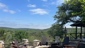 An outdoor seating area with stone fire pit and wooden chairs, overlooking a forested landscape. - Stay at these upscale, historic cabins set in New Braunfels near Guadalupe River (New Braunfels)