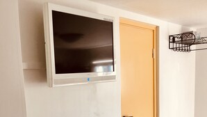 A room with a mounted TV, a white console with drawers, a yellow door, and a metal shelf unit.