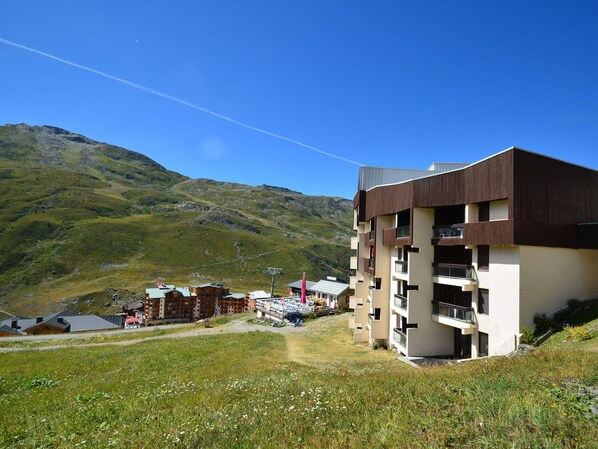 A modern building with a flat roof and multiple balconies, surrounded by a mountainous landscape.
