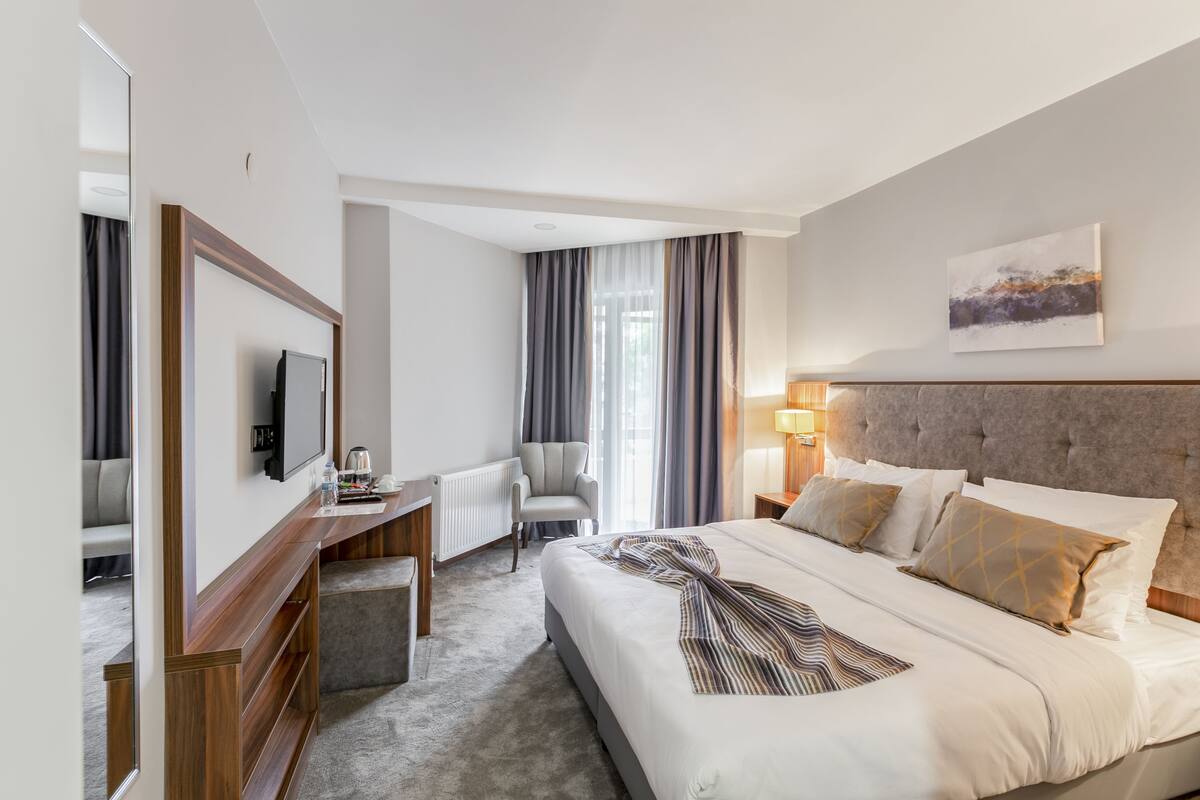 A hotel room with a large bed, a desk with a chair, a television, and a window with curtains.