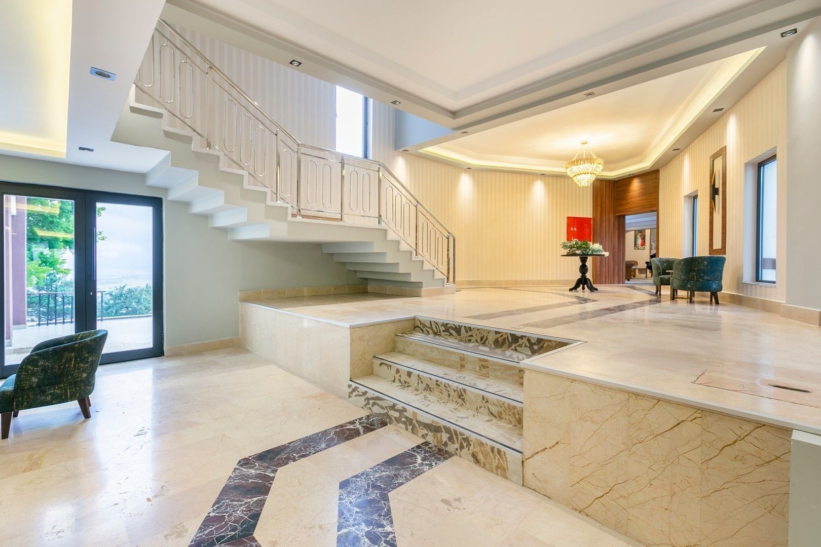 Eine großzügige Lobby mit einer Marmortreppe, einem Chandelier und Blick ins Freie.