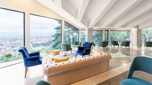 Un vaste espace de vie doté d’une grande fenêtre offrant une vue sur la ville, d’un canapé confortable et de plusieurs fauteuils.