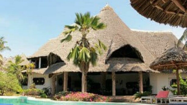 Un resort con piscina, edificios de techo de paja y palmeras.