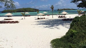 Una playa de arena blanca, con varias sombrillas y sillas de playa.