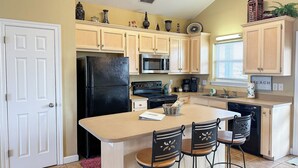 Una cocina compacta con una isla central, armarios de madera, un refrigerador negro, un microondas y una cafetera.
