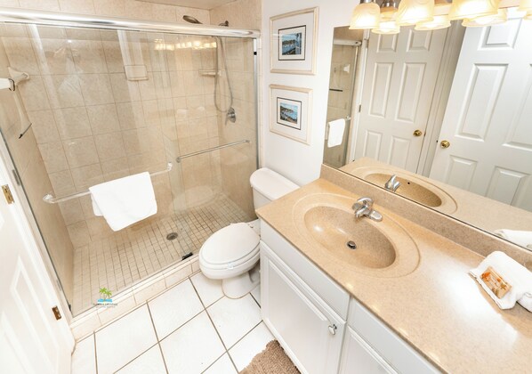 A modern bathroom with a glass-enclosed shower, a white toilet, a beige sink, and a large mirror.