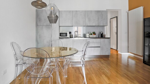 A modern kitchen with grey cabinets, a microwave, and a coffee machine. There is a glass dining table with clear chairs. - Le Porte, Luxury apartment UNIQUE TOWERS VIEW (Bologna)