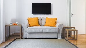A living room with a grey sofa, two yellow cushions, a flat-screen TV, a small wooden side table, and a grey rug. - Le Porte, Luxury apartment UNIQUE TOWERS VIEW (Bologna)
