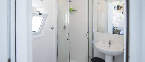 A modern bathroom with a glass shower enclosure, a white sink, and a small stool.