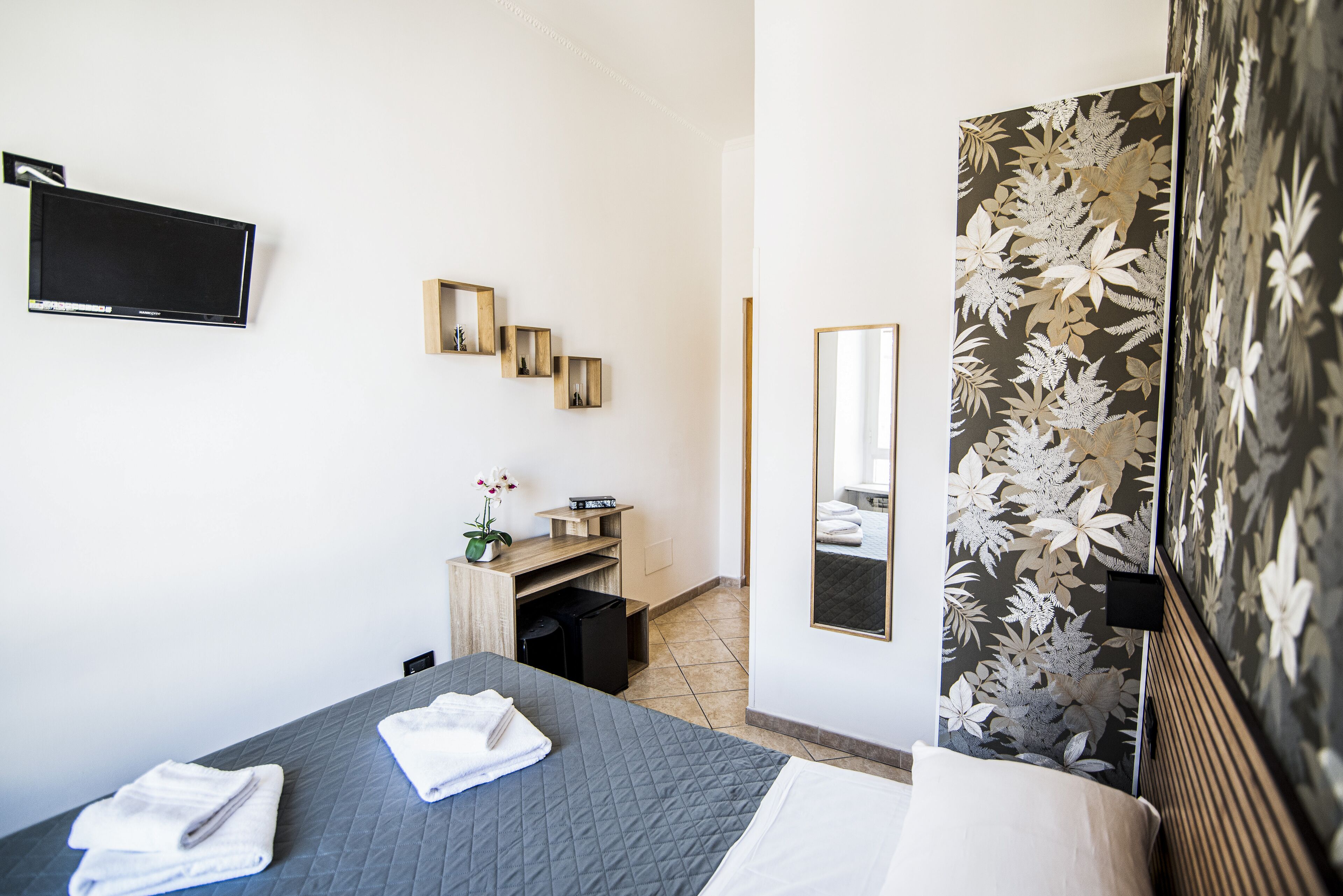 Habitación de hotel con cama, televisor de pantalla plana en la pared, escritorio pequeño con planta y espejo.