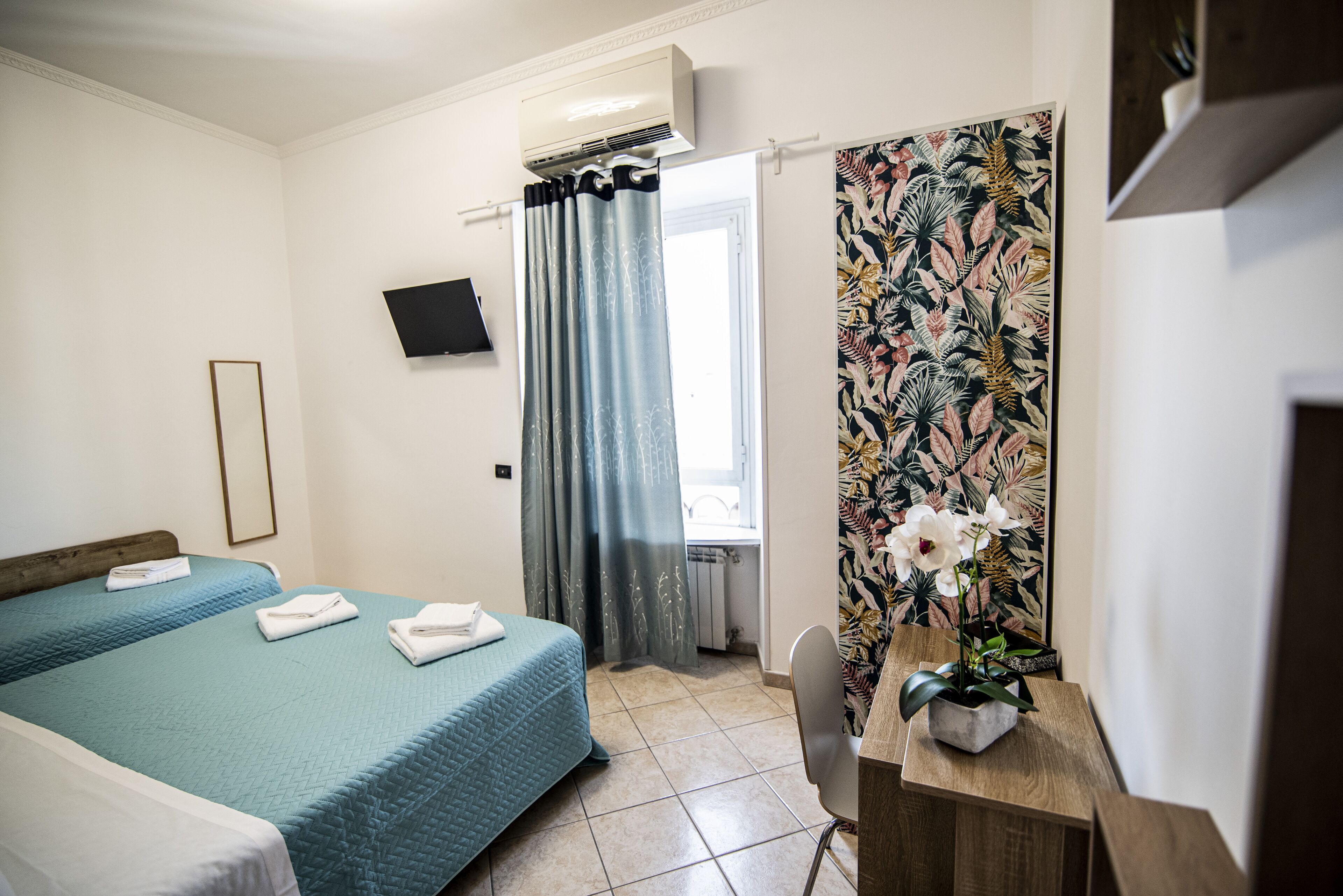 A hotel room with two beds, a desk, a chair, a TV, and a window with curtains.