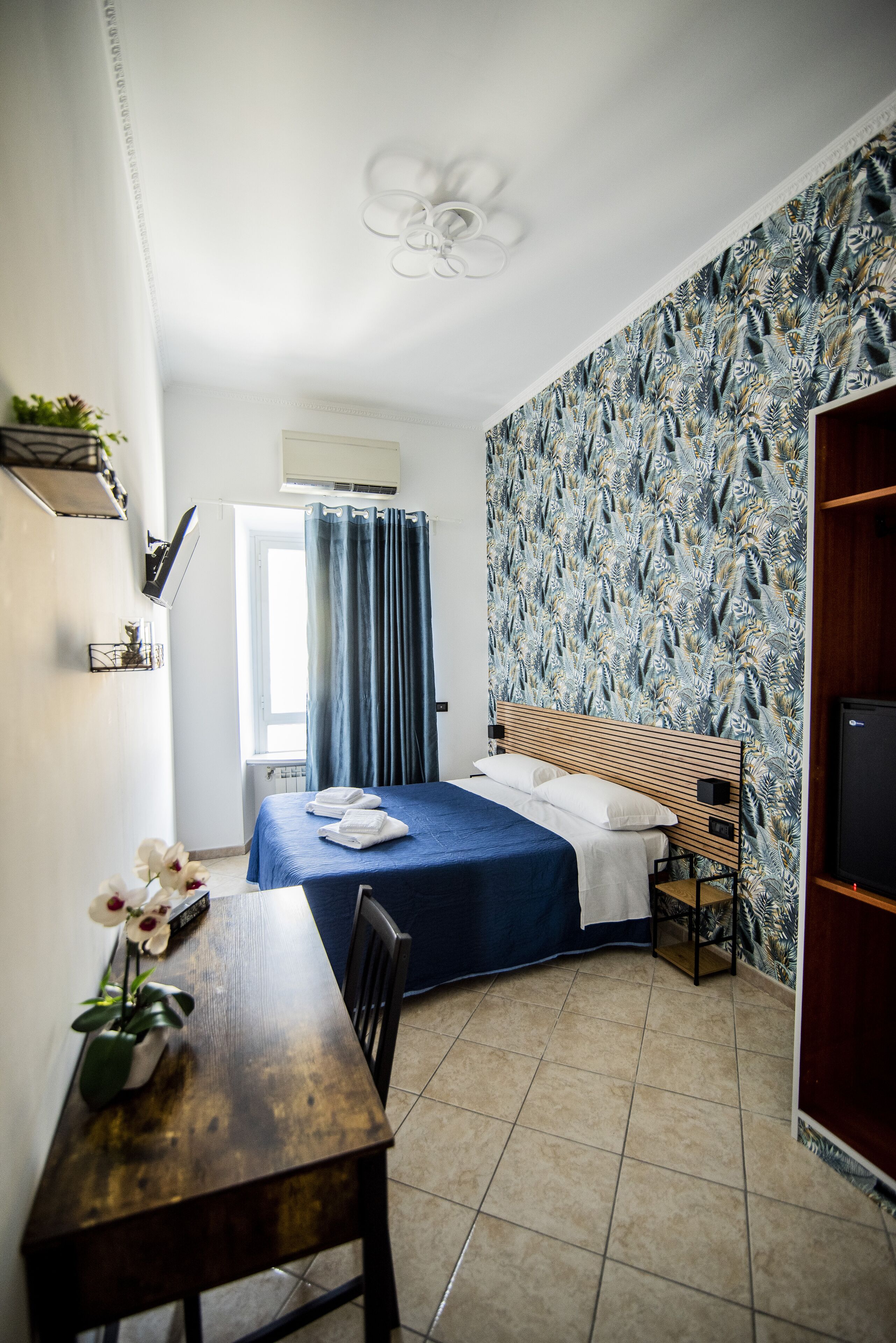 Une chambre à coucher avec un lit, un bureau, une chaise, une télévision et une fenêtre avec des rideaux.