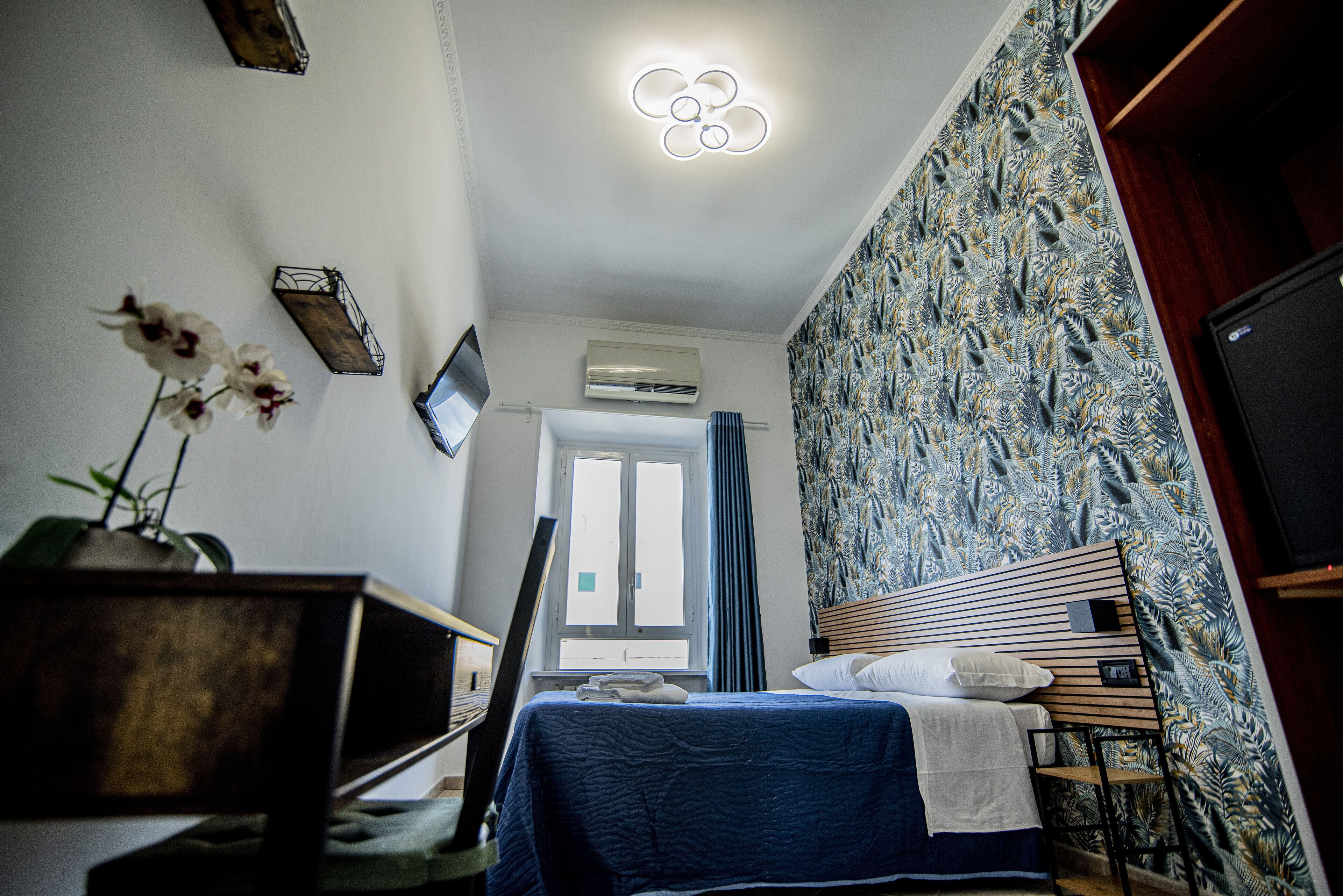 A bedroom with a bed, a desk, a TV, and a window.