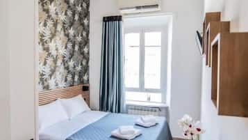 Ein Hotelzimmer mit Bett, Schreibtisch, einem Fenster mit Vorhängen, einer Wand mit Blumenmuster und einer Deckenleuchte.