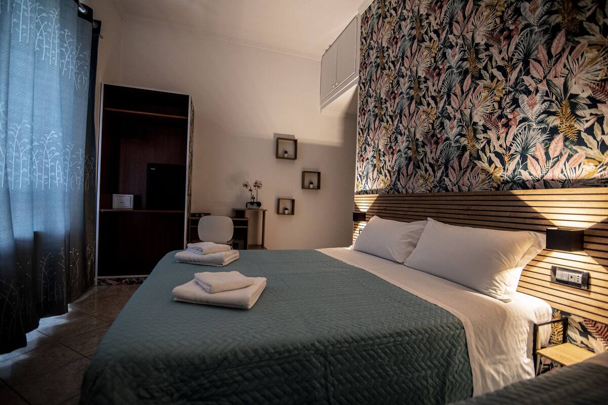 A hotel room with a bed, a nightstand, a desk, a chair, a wardrobe, and a shower area.