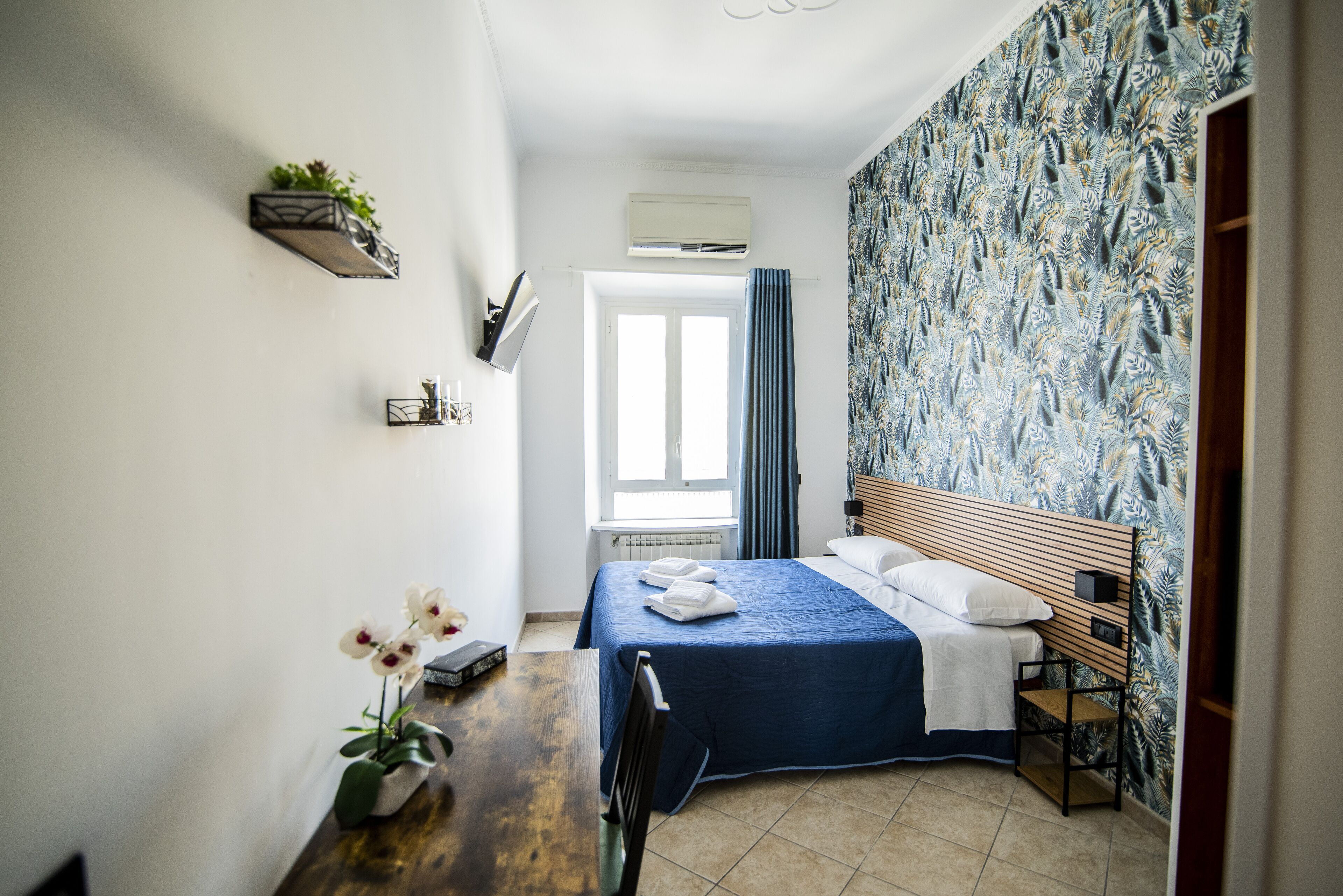 A bedroom with a bed, a desk, a chair, a window, and a wall-mounted air conditioner.