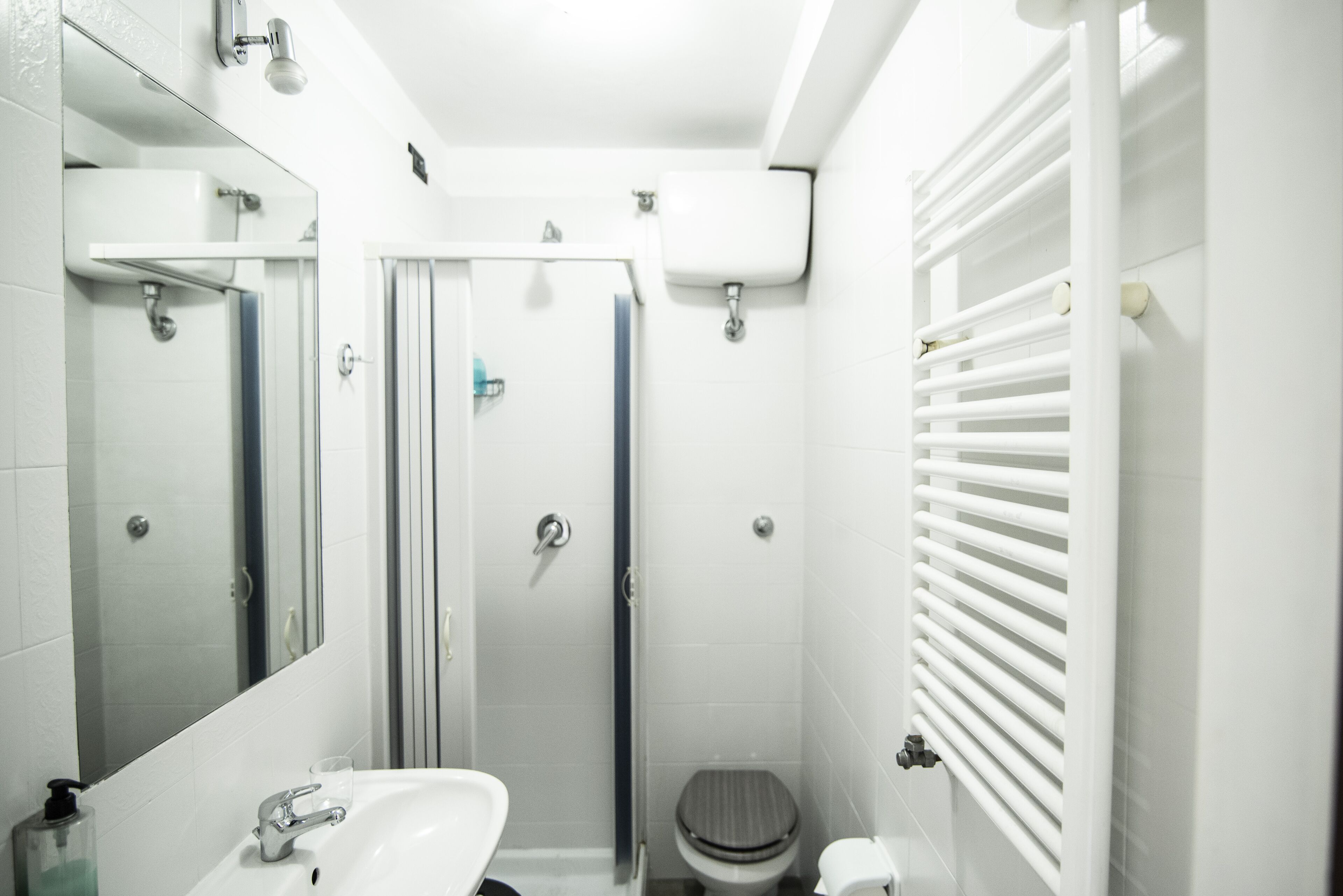 A modern bathroom with a sink, mirror, shower, toilet, and a radiator.