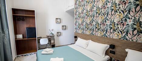 A hotel room with two beds, a wooden wardrobe, a desk with a chair, and a floral-patterned wall.
