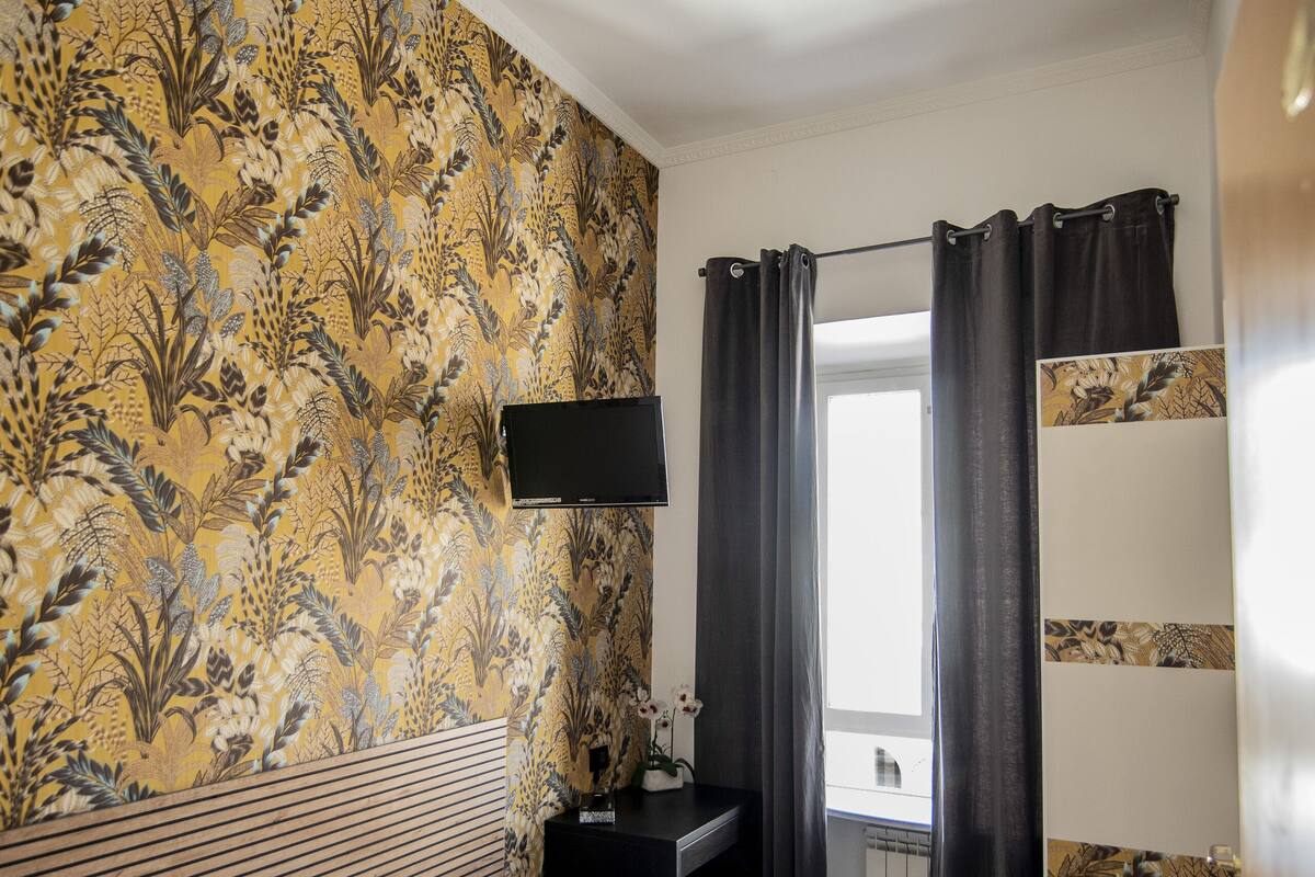 A hotel room with a bed, a desk, a flat-screen TV, and a window with curtains.