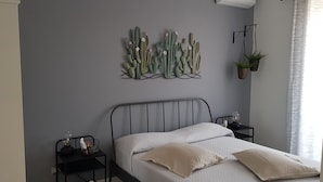 Un dormitorio con una cama, dos mesitas de noche, un cactus decorativo en la pared y una planta colgante.